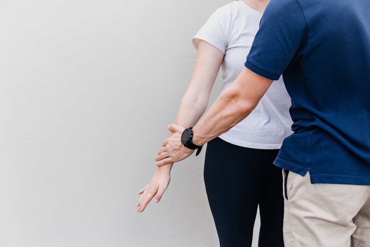 Comprehensive Physical Assessment & Testing. A physical therapist conducts manual muscle testing by pressing on the patient's arm just above the wrist as they move their arm away from their body.
