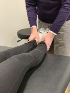 a female lying on a treatment table has her legs held by a physical therapist to evaluate her functional leg length discrepancy.